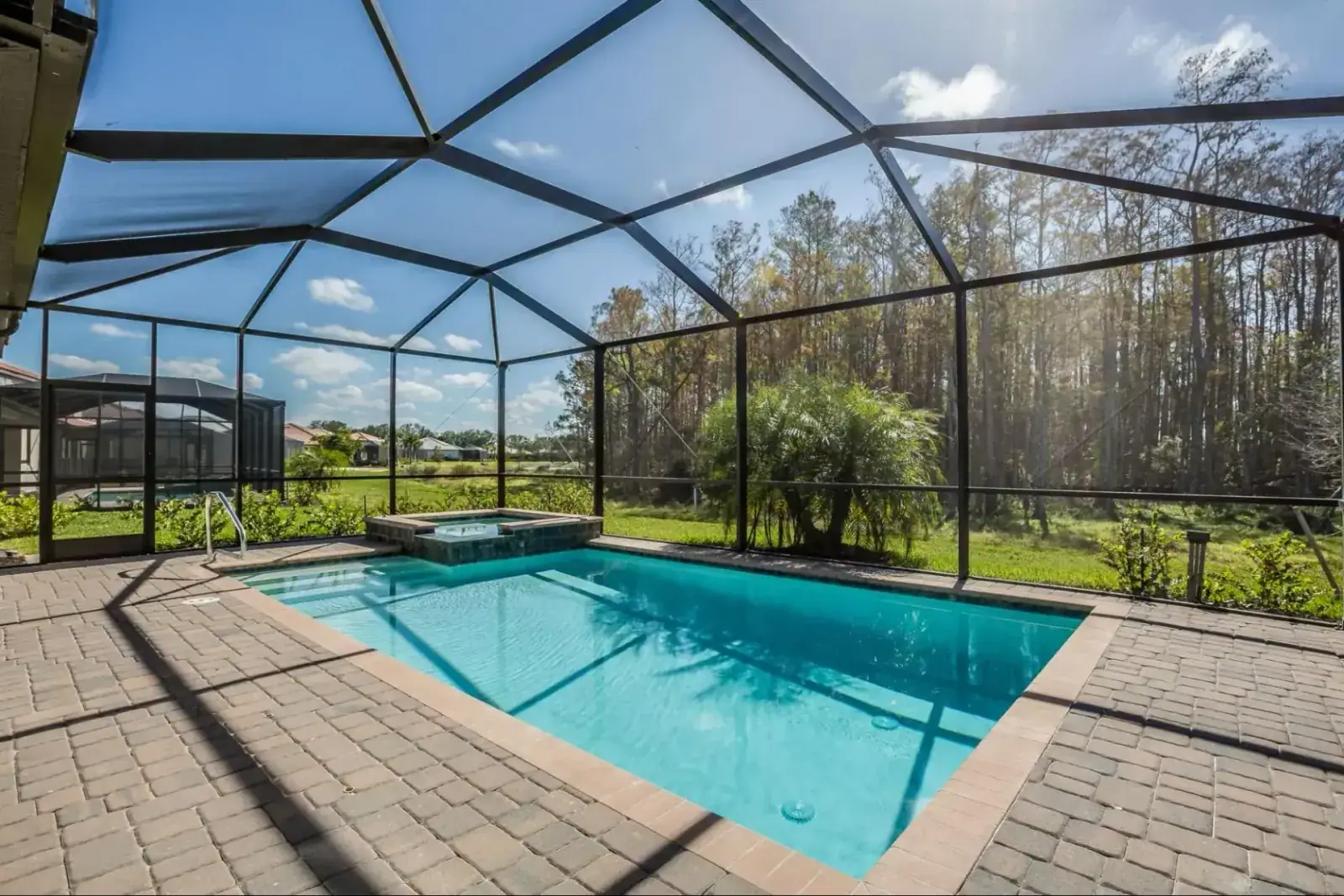 Aluminum screen enclosure over a backyard pool and spa with paver deck