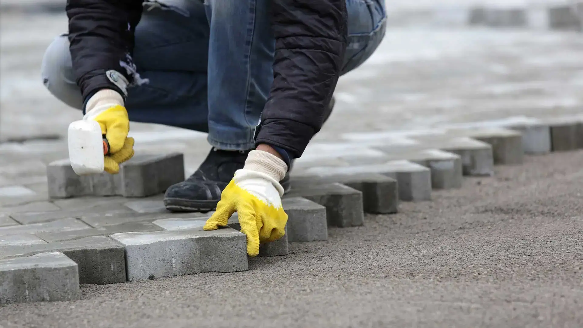 Installer setting a concrete paver into a sand bed on a new paver surface